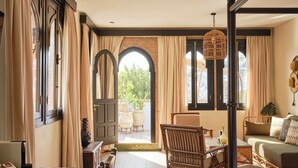 Un dormitorio espacioso con una cama grande, un comedor con una mesa y sillas de madera, y vistas a través de un ventanal de arco.