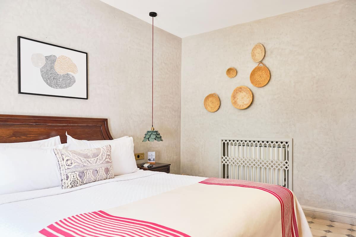 A bedroom with a bed, pillows, a nightstand, a wall-mounted light, and decorative wall art.