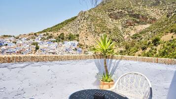 Una terraza con una mesa y sillas, con vistas a un pueblo costero de edificios azules y montañas al fondo.