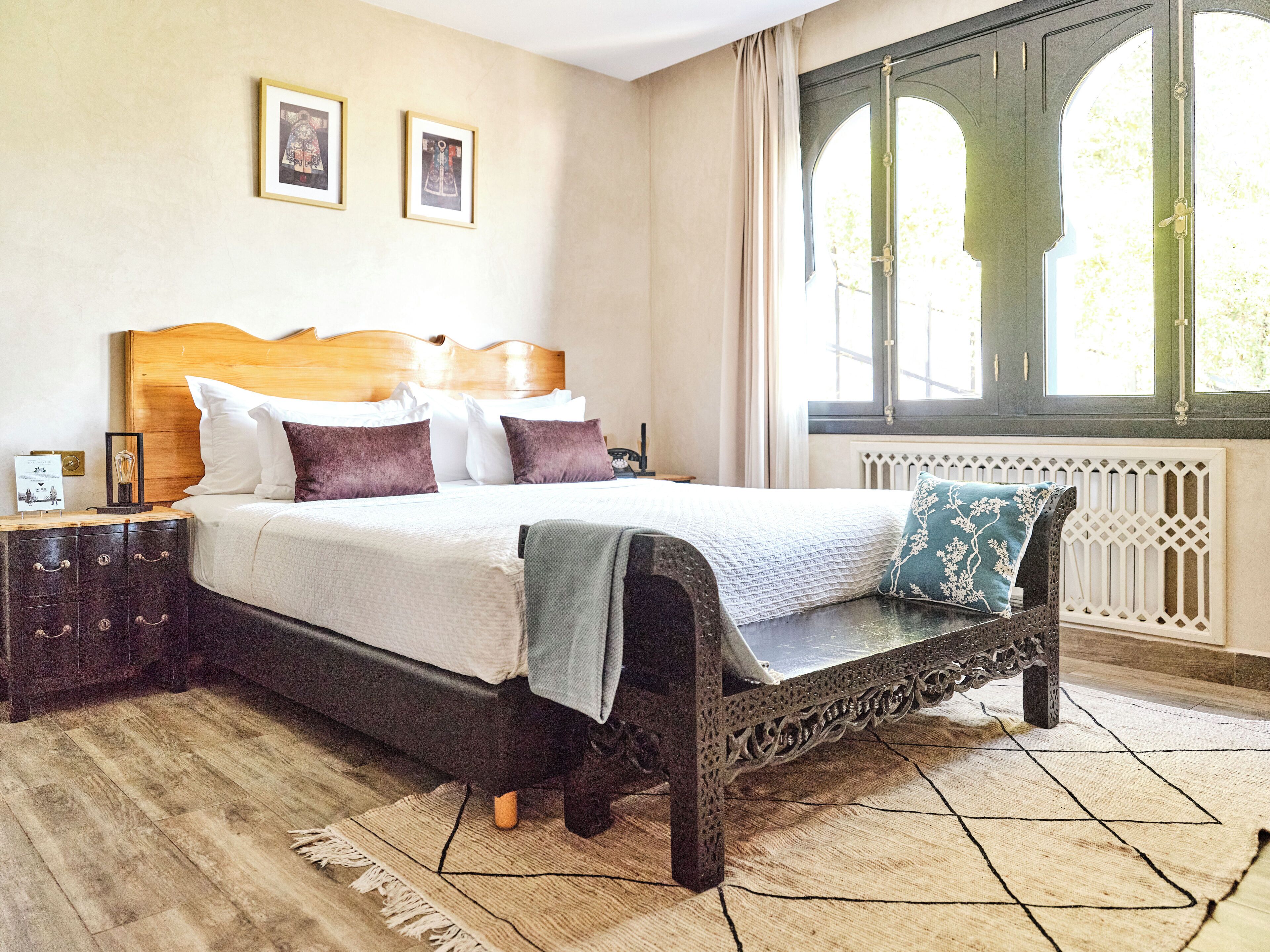 A bedroom with a wooden bed, a nightstand, a dresser, and a large window with a view of greenery.