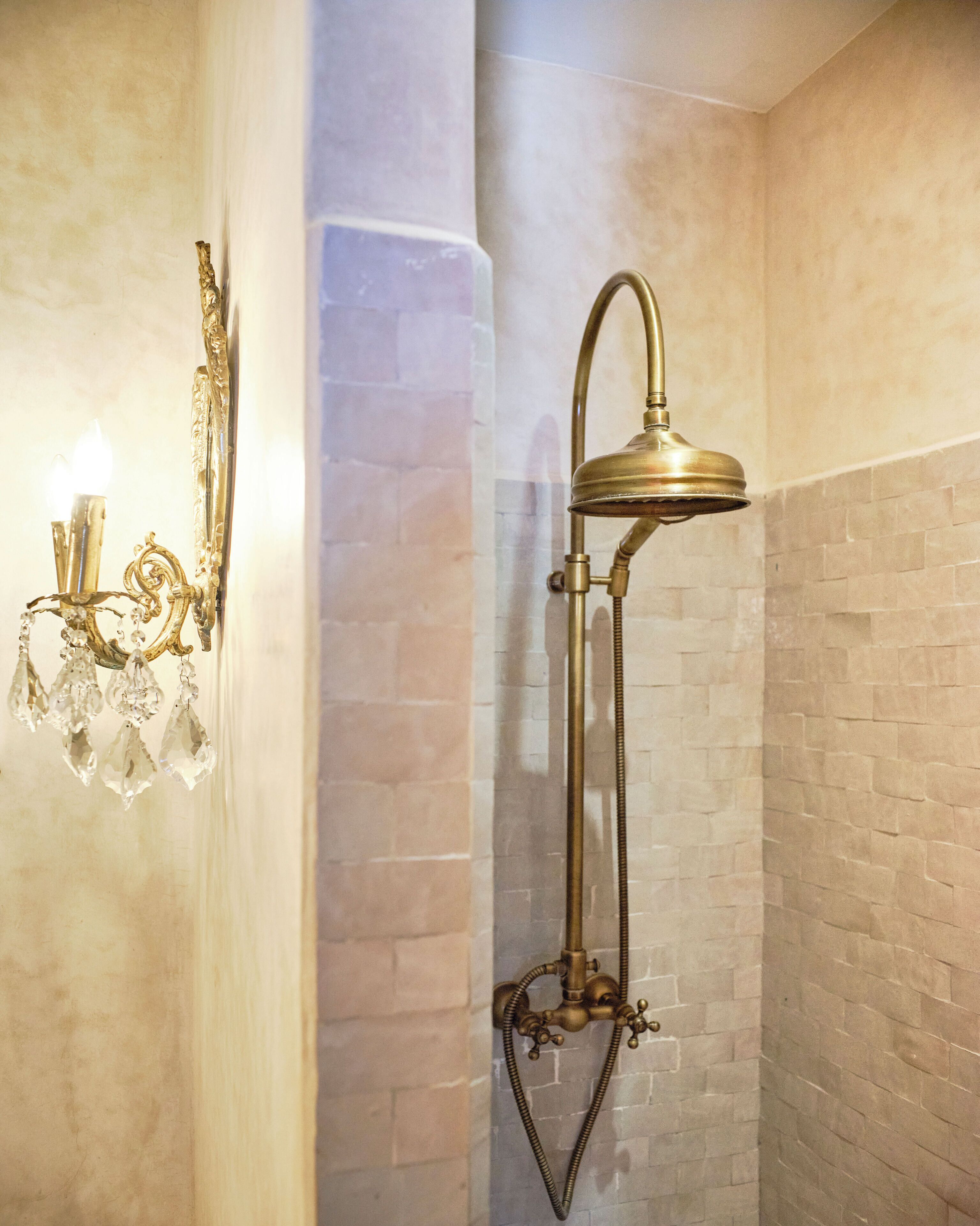 A bathroom with a wall-mounted shower, a wall sconce, and a crystal chandelier.