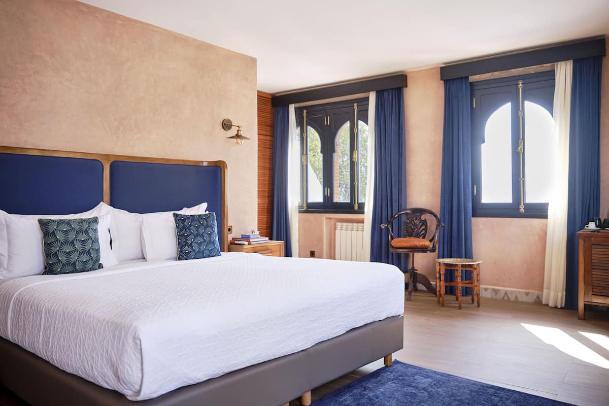 A bedroom with a large bed, a nightstand, a chair, and a window with curtains.