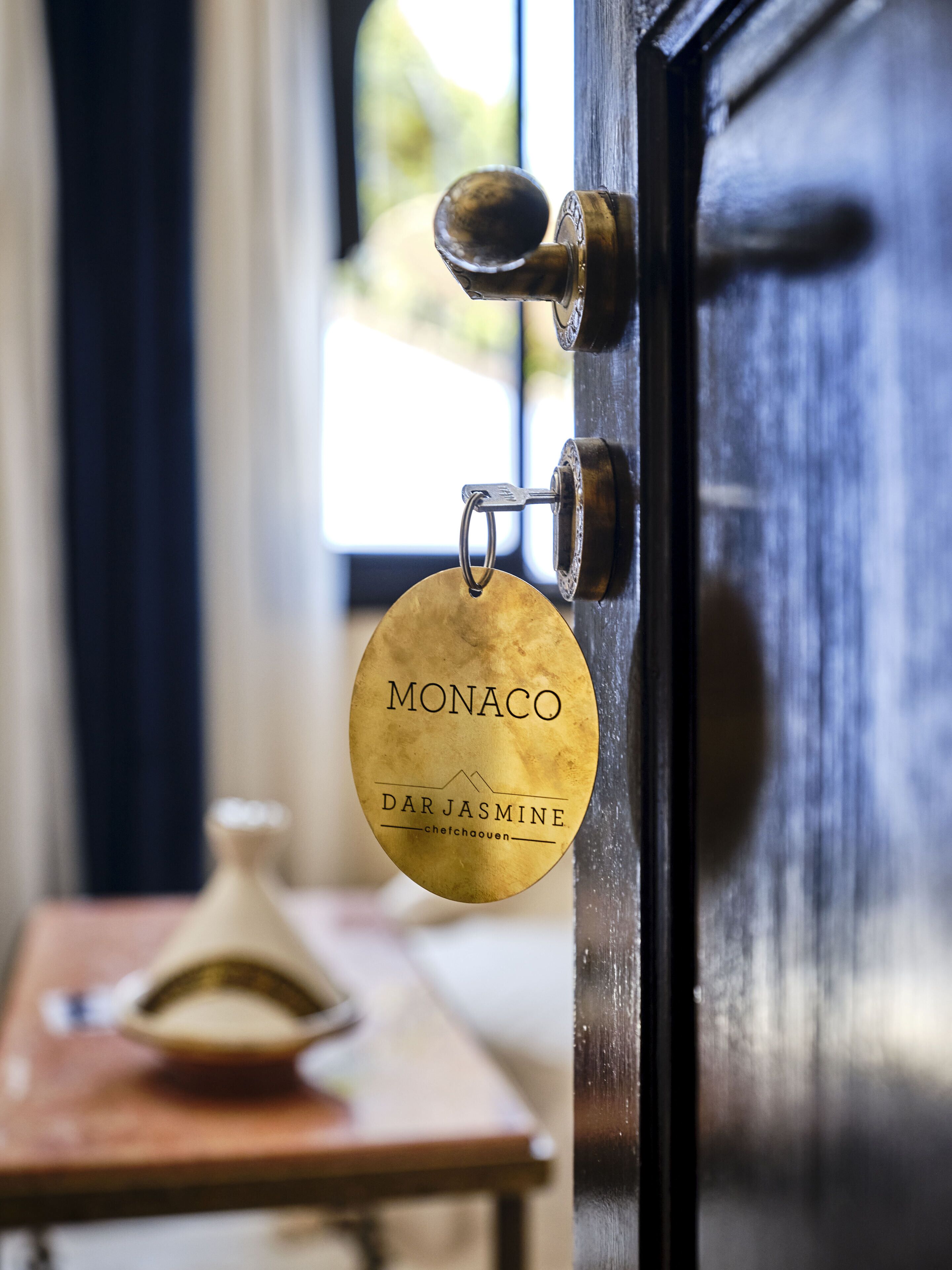 A door with a brass keyring and a key, a wooden table with a vase, and a window with daylight.