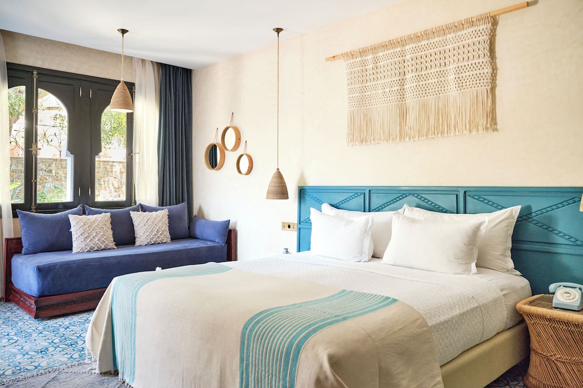 A bedroom with a large bed, a sofa, and a macrame wall hanging.