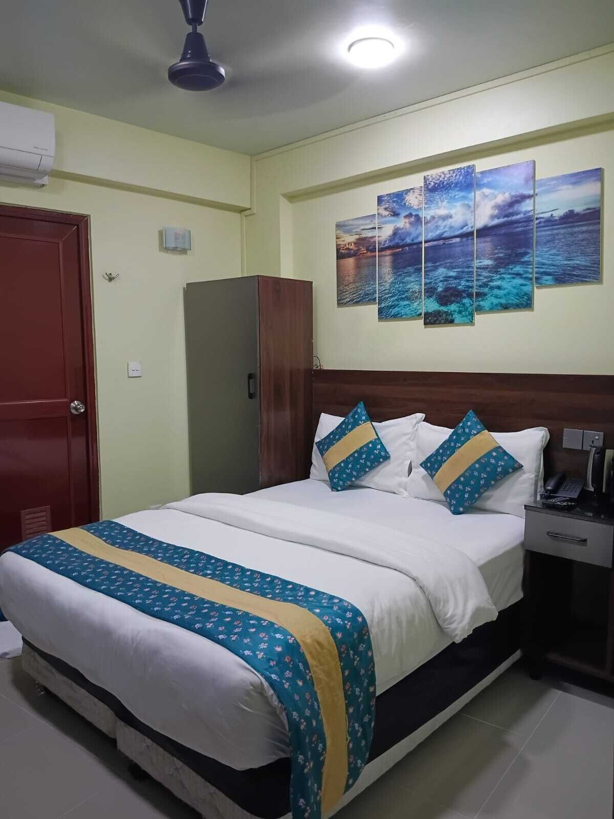 Una cama bien hecha con una colcha azul y amarilla, un cabecero de madera y una mesita de noche con un teléfono y una lámpara.