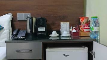 Una habitación de hotel con cama, escritorio, teléfono, cafetera, refrigerador pequeño y algunos alimentos.