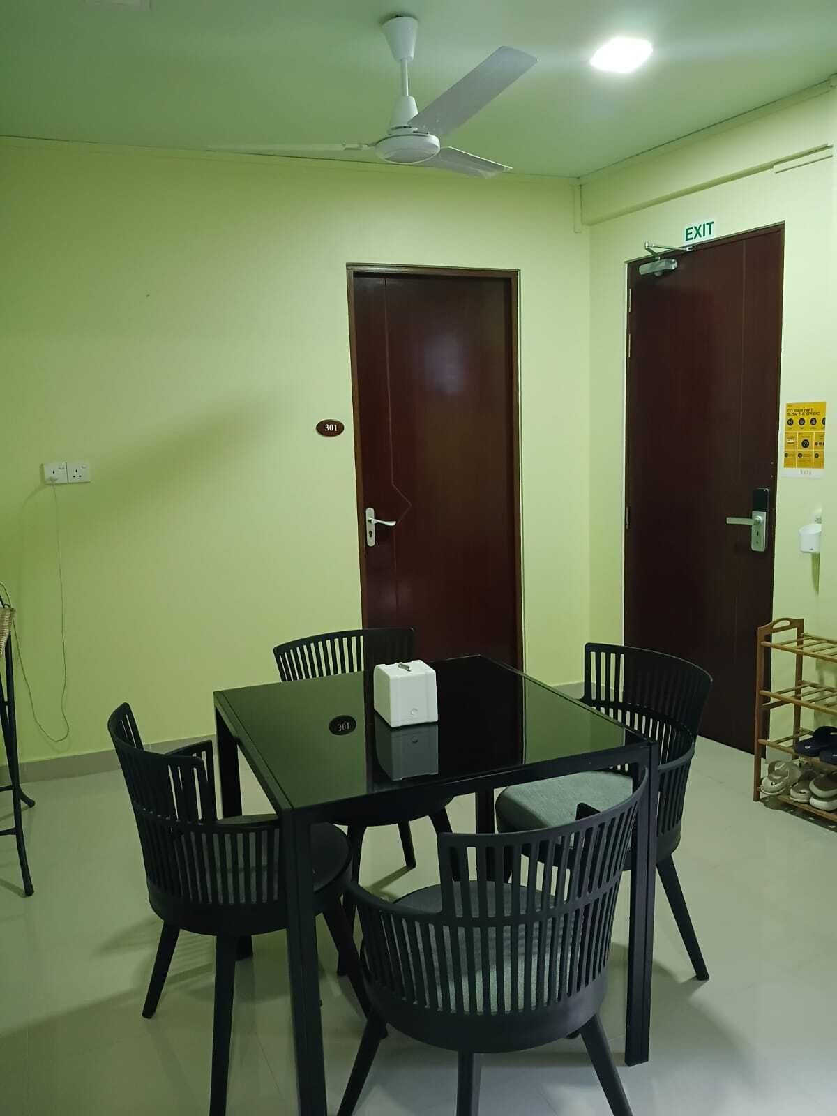 Una sala de conferencias con una mesa de vidrio, sillas negras, un ventilador de techo y dos puertas con números de sala.