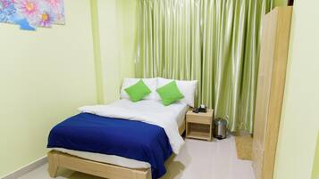 A bedroom with a bed, green pillows, a nightstand, a trash bin, and a wardrobe.