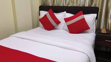 Una cama con ropa de cama blanca y almohadas rojas y blancas, un cabecero de madera y una cortina dorada al fondo.