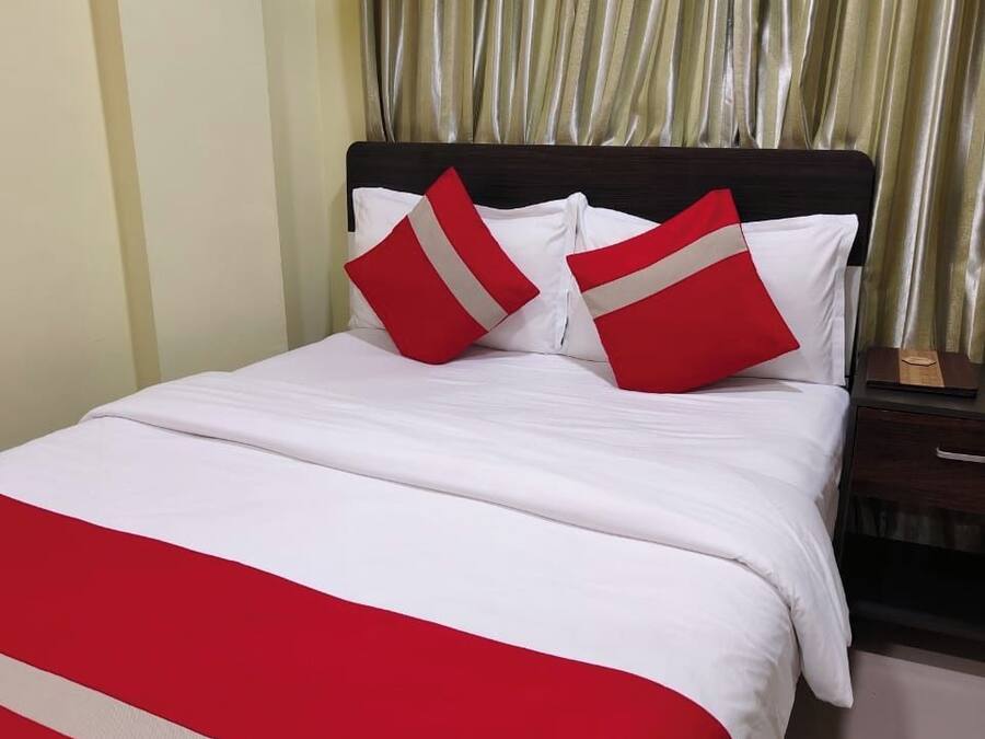 Una cama con ropa de cama blanca y almohadas rojas y blancas, un cabecero de madera y una cortina dorada al fondo.
