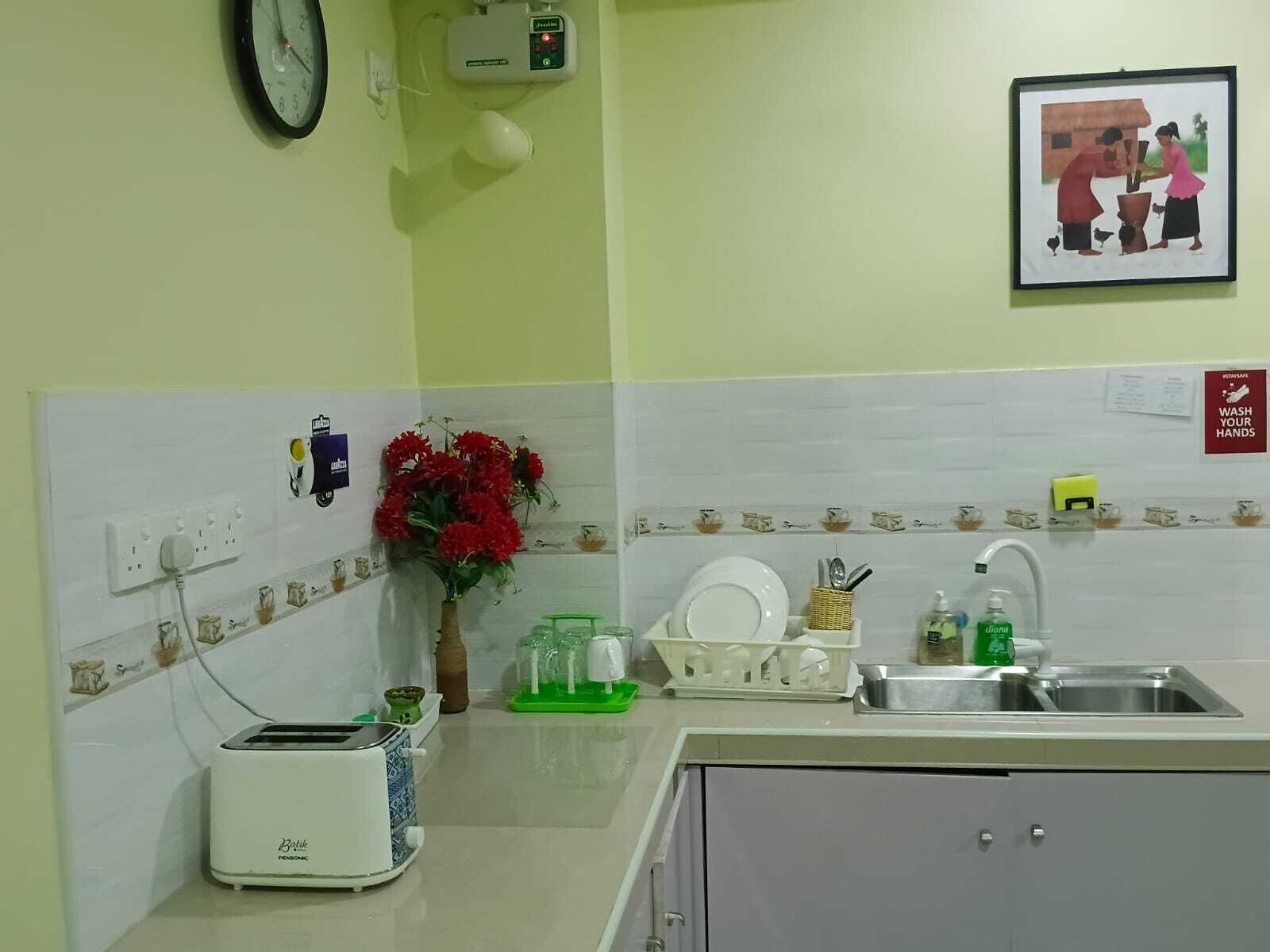 Una cocina con un tostador, un lavamanos, un reloj, un cuadro en la pared y un florero con flores.
