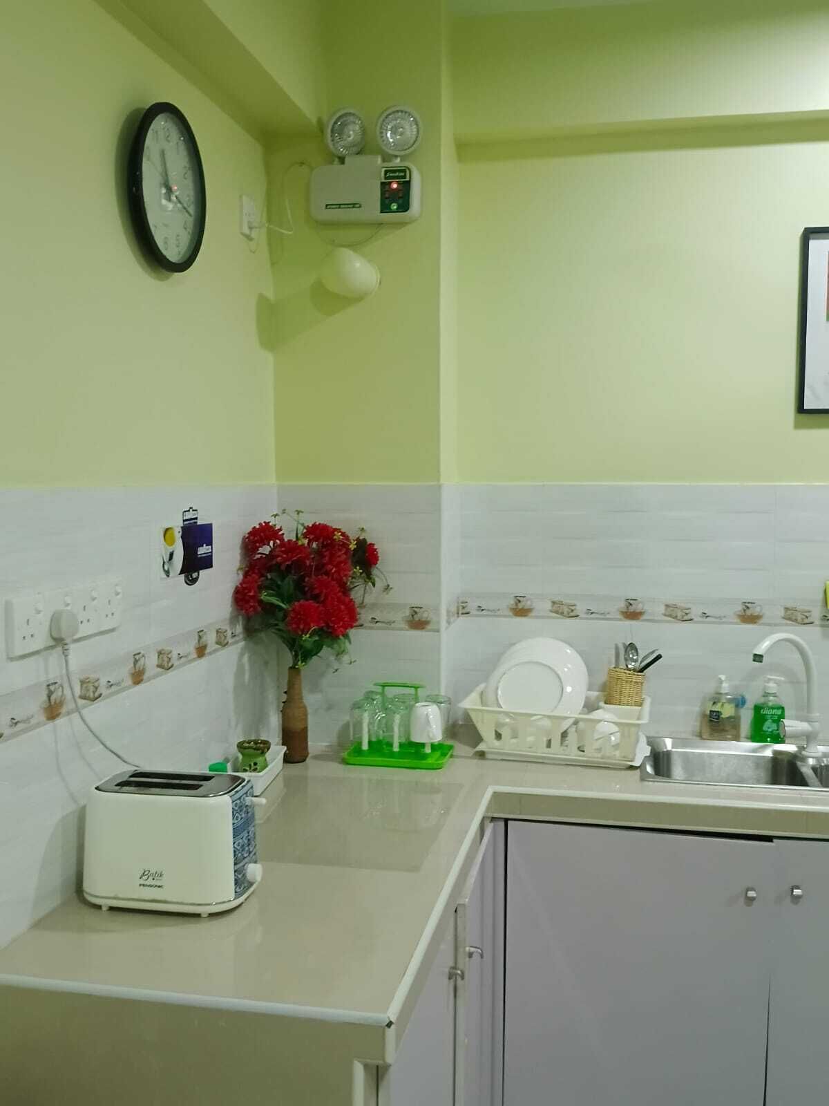 A kitchen with a clock, a fan, a toaster, and a vase with flowers.