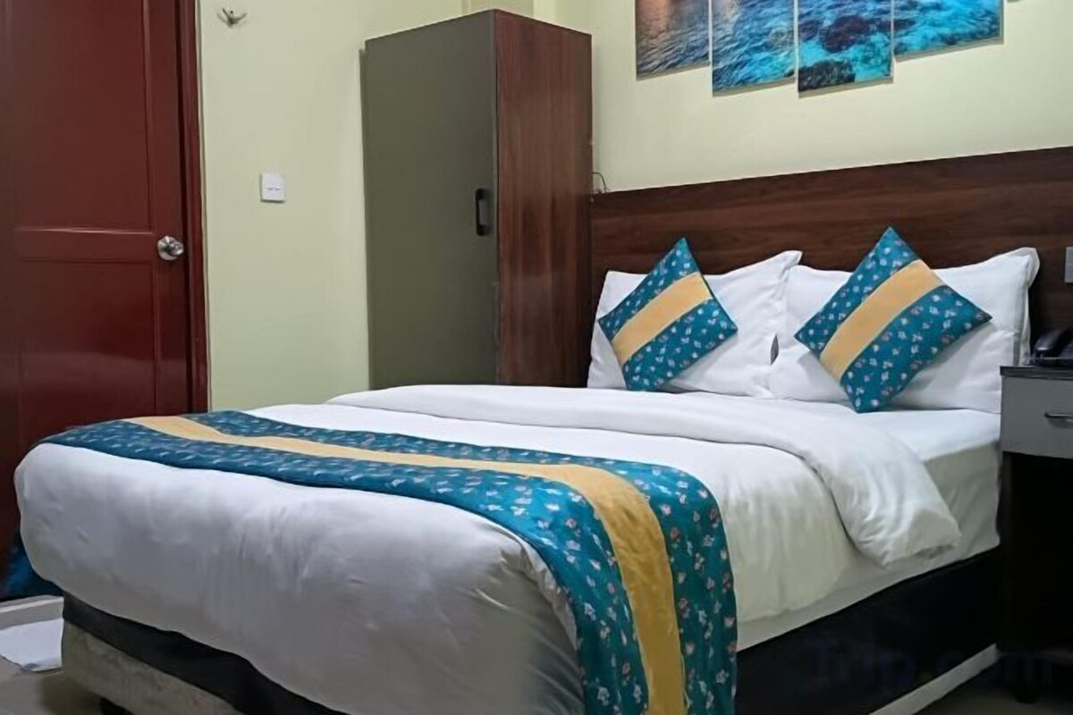 Una cama con colcha blanca y azul, dos almohadas a rayas azules y amarillas, y un cabecero de madera.