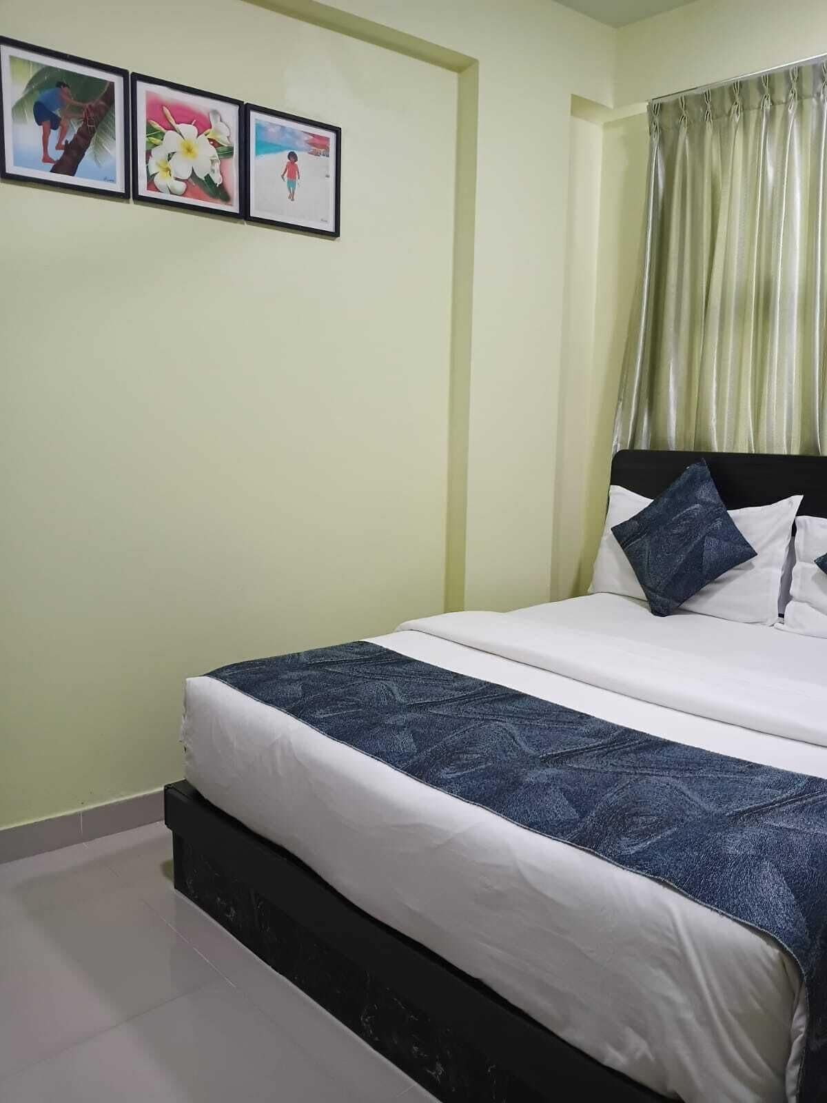 Quarto com cama, cabeceira, janela com cortinas e três quadros na parede.