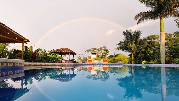 A clear pool with a rainbow, surrounded by tropical plants and a gazebo. - Hacienda Hotel El Percal (Montenegro)