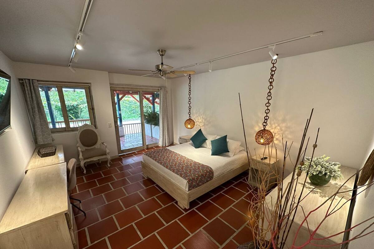 Un dormitorio con cama, escritorio, silla, ventilador de techo y vista al exterior.