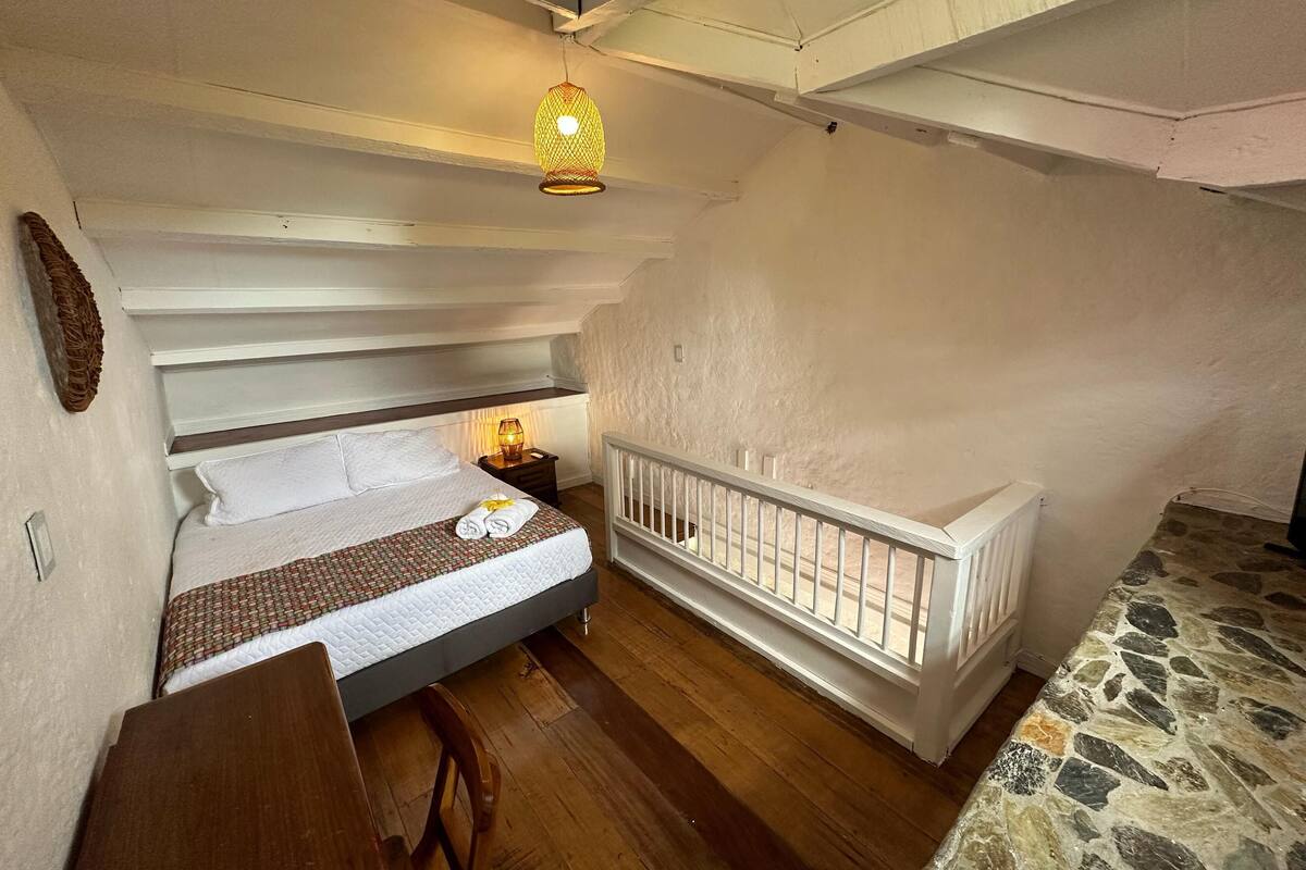 Un dormitorio con cama, mesita de noche, lámpara y barandilla blanca.