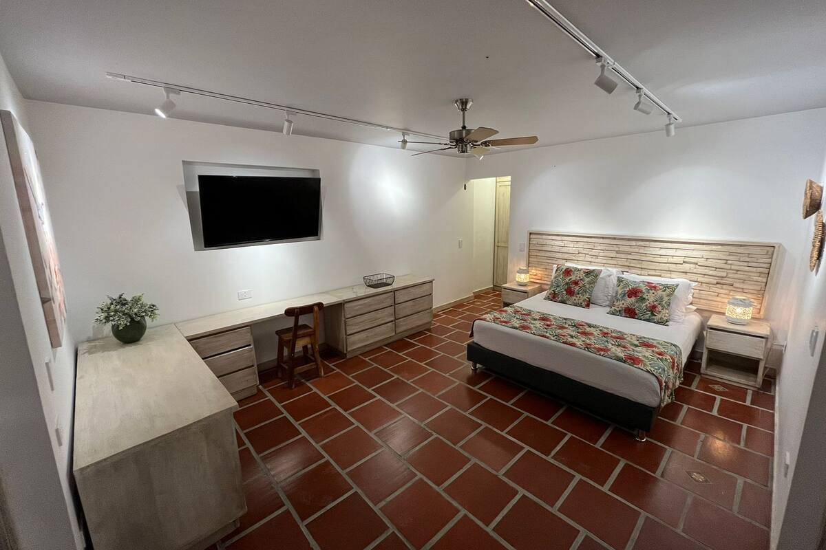 Un dormitorio con cama, escritorio, silla, televisor y ventilador de techo.