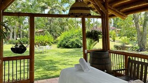 A room with a bed, a wooden bench, and a view of a garden with palm trees. - Hacienda Hotel El Percal (Montenegro)