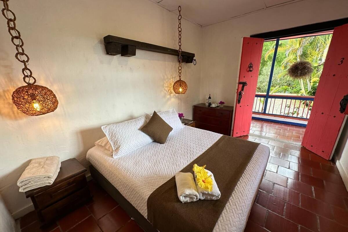 Un dormitorio con cama, mesitas de noche, una lámpara colgante y vistas al exterior a través de una puerta.