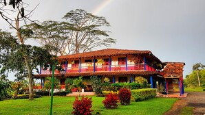 A two-story building with a red-tiled roof and balconies, surrounded by lush greenery and a visible rainbow. - Hacienda Hotel El Percal (Montenegro)