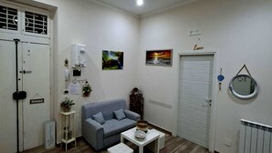 Un espacio habitable compacto con un sofá gris, una mesita blanca y un radiador blanco.