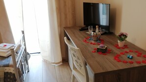 Una mesa de madera para comer con una televisión, copas de champán y una vela.