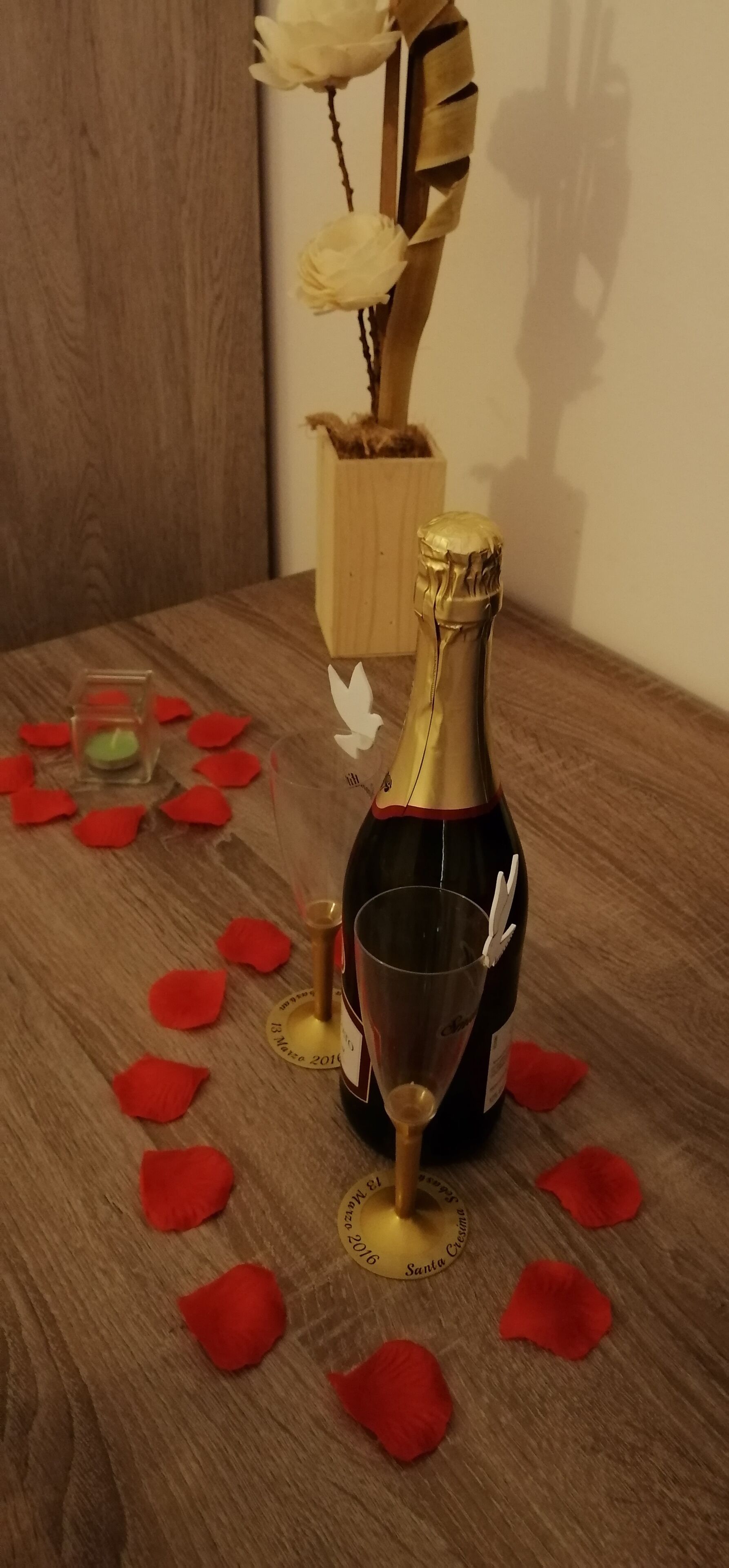 Eine Champagnerflasche, ein Glas und rote Rosenblätter auf einem Holztisch.