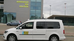 Una furgoneta blanca estacionada frente a un edificio con grandes ventanales y un letrero que dice "BRINDISI AEROPORTO DEL SALENTO".