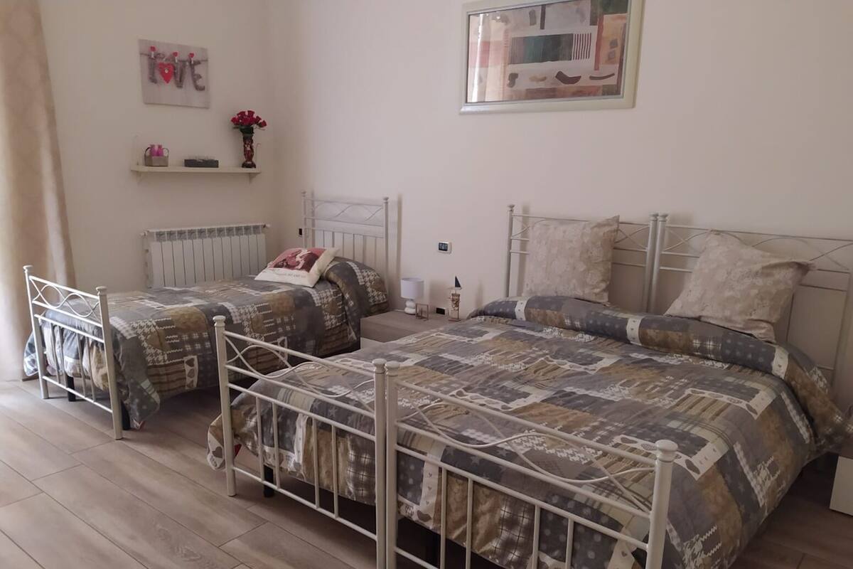 A bedroom with two single beds, a radiator, a shelf with decorative items, and a framed picture on the wall.