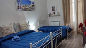 Una habitación de hotel con dos camas, un radiador, una ventana con cortinas y una repisa de pared con objetos decorativos.