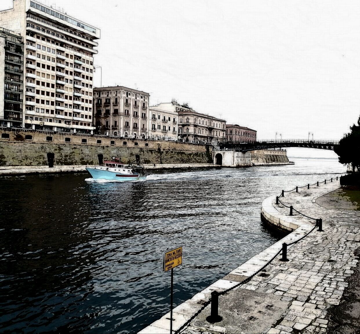A river with a boat, a stone walkway, and buildings along the riverbank.