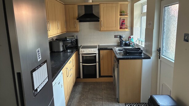 A compact kitchen with wooden cabinets, a Bosch refrigerator, a microwave, a stove, and a sink. - SOUTH LAKES TOWN CENTRE HOUSE (Barrow-in-Furness)