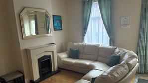 A living room with a beige sectional sofa, a fireplace, a bench, and a large mirror. - SOUTH LAKES TOWN CENTRE HOUSE (Barrow-in-Furness)