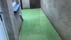 A narrow corridor with artificial green carpet, concrete walls, and a dark wooden door. - SOUTH LAKES TOWN CENTRE HOUSE (Barrow-in-Furness)