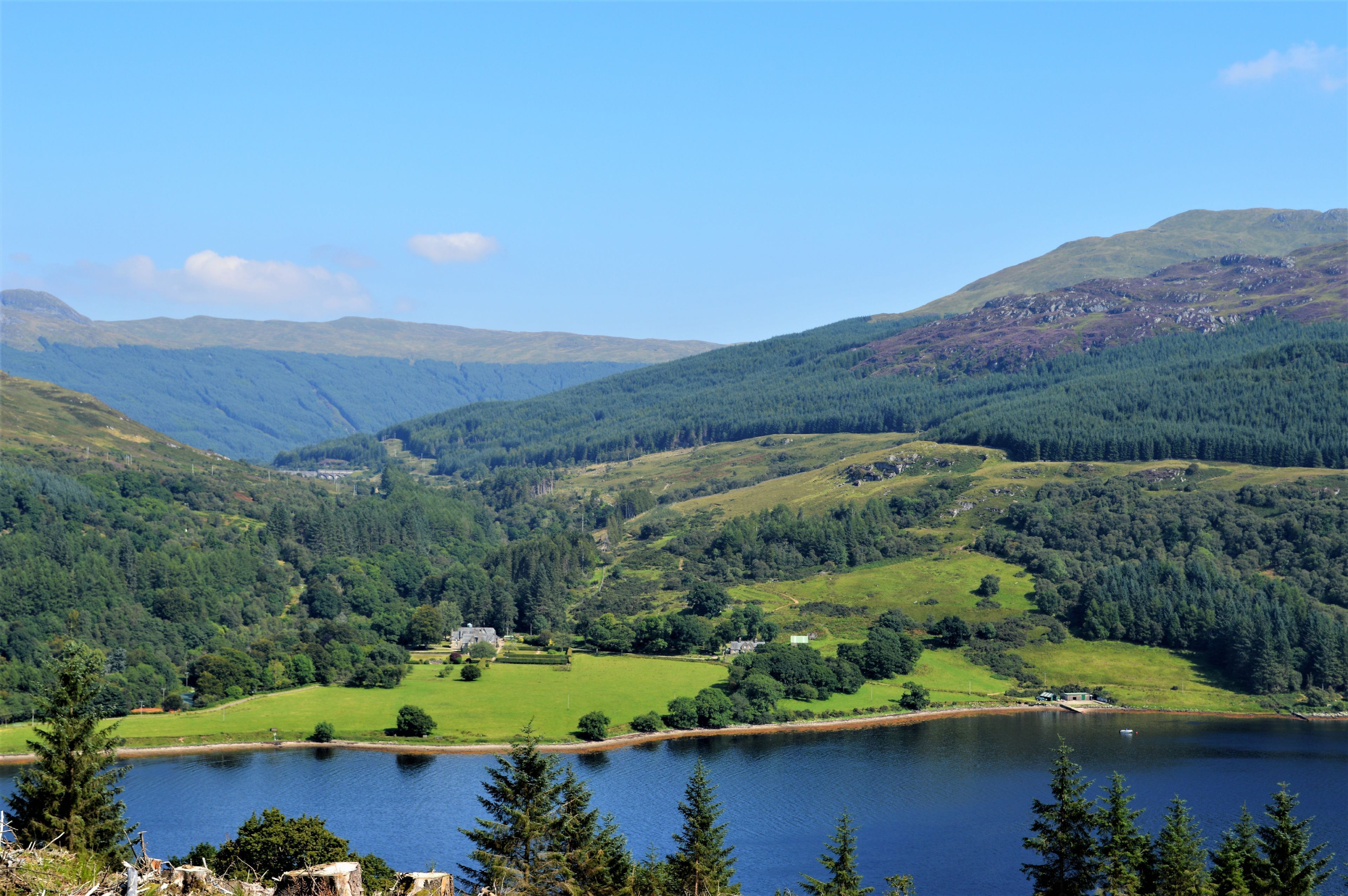 A scenic view of a lake surrounded by lush green hills and a clear blue sky.