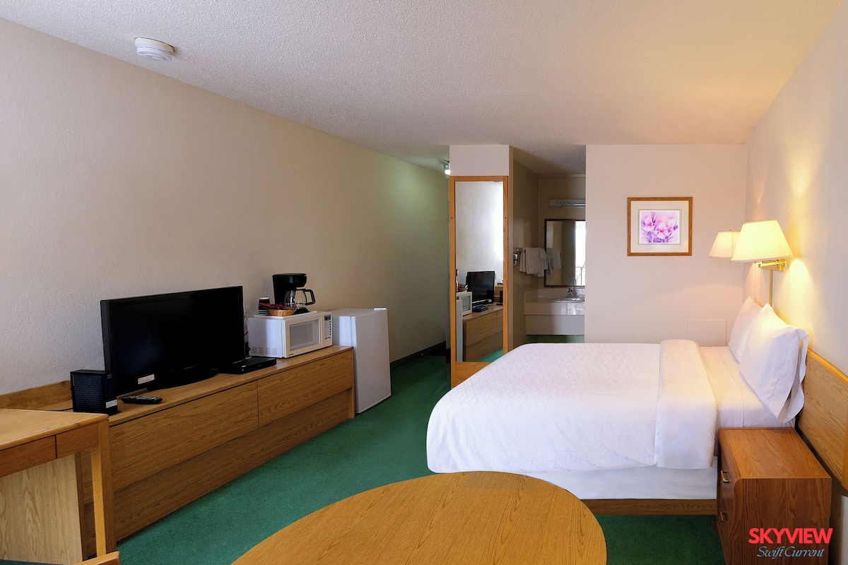 A hotel room with a bed, a desk with a television, a microwave, and a coffee maker.
