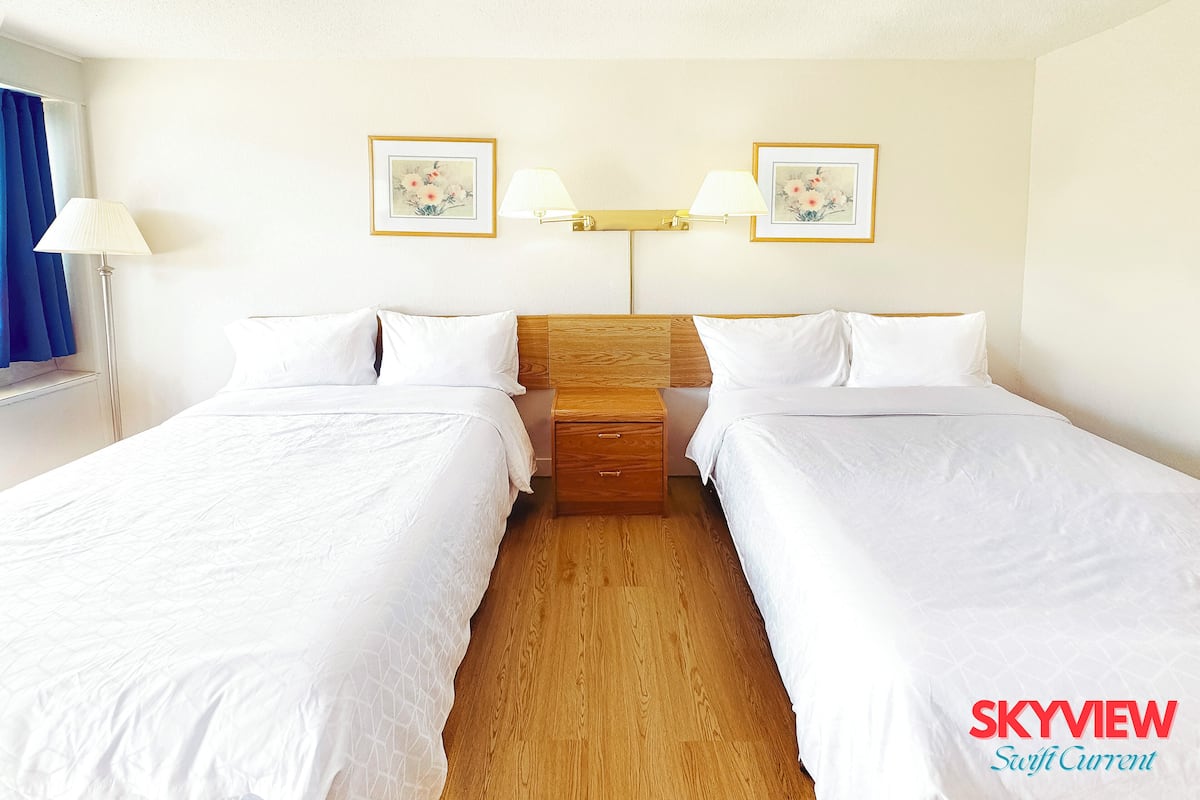 A hotel room with two single beds, a wooden nightstand, a lamp, and two wall-mounted lamps.