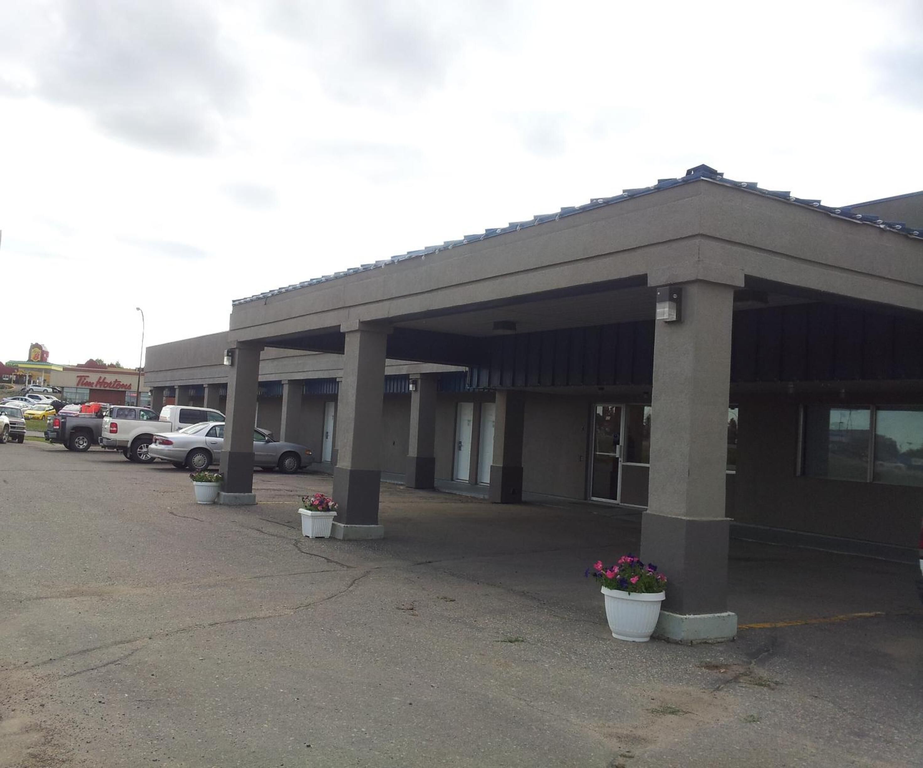 A building with a covered parking area, multiple columns, and potted plants.