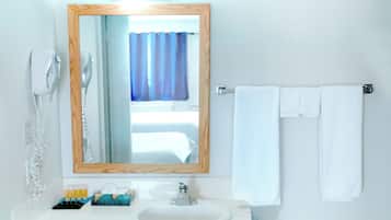 Un baño con espejo de marco de madera, lavamanos blanco, toallero con dos toallas blancas, secador de pelo y ventana con cortinas azules.