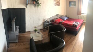 A room with a bed, a chair, a small table with a plant, and a TV. - Pension Lume (Oberraden)