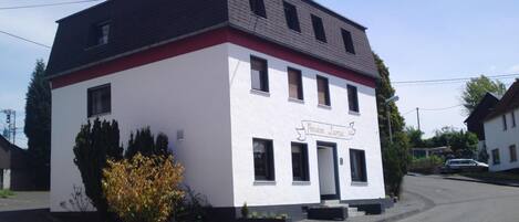 A two-story building with a white facade and a red trim. The sign on the building reads "Pension Lume."