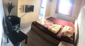 A bedroom with a bed, a chair, a small table, a TV, and a potted plant. - Pension Lume (Oberraden)