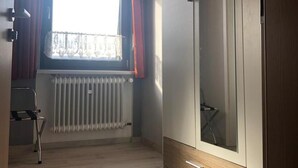 A room with a wooden ceiling, a radiator, a window with curtains, and a wardrobe with drawers. - Pension Lume (Oberraden)