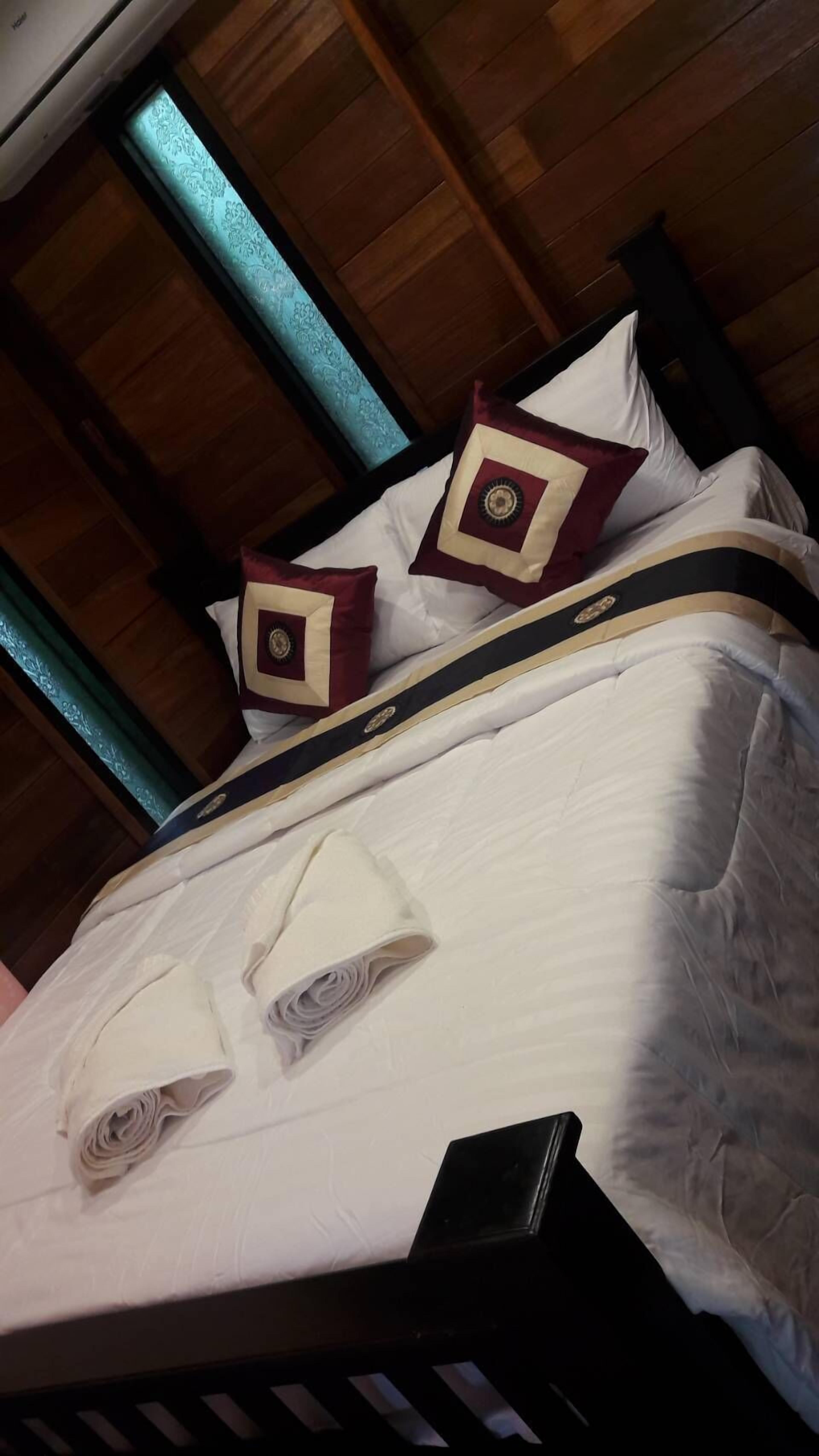 Un lit recouvert d’une couverture blanche, agrémenté de deux coussins décoratifs et d’une serviette blanche pliée.