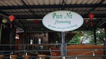 Une enseigne indiquant « Pun Na Homestay » avec le message : « Nous prendrons soin de vous comme si vous étiez de la famille. »