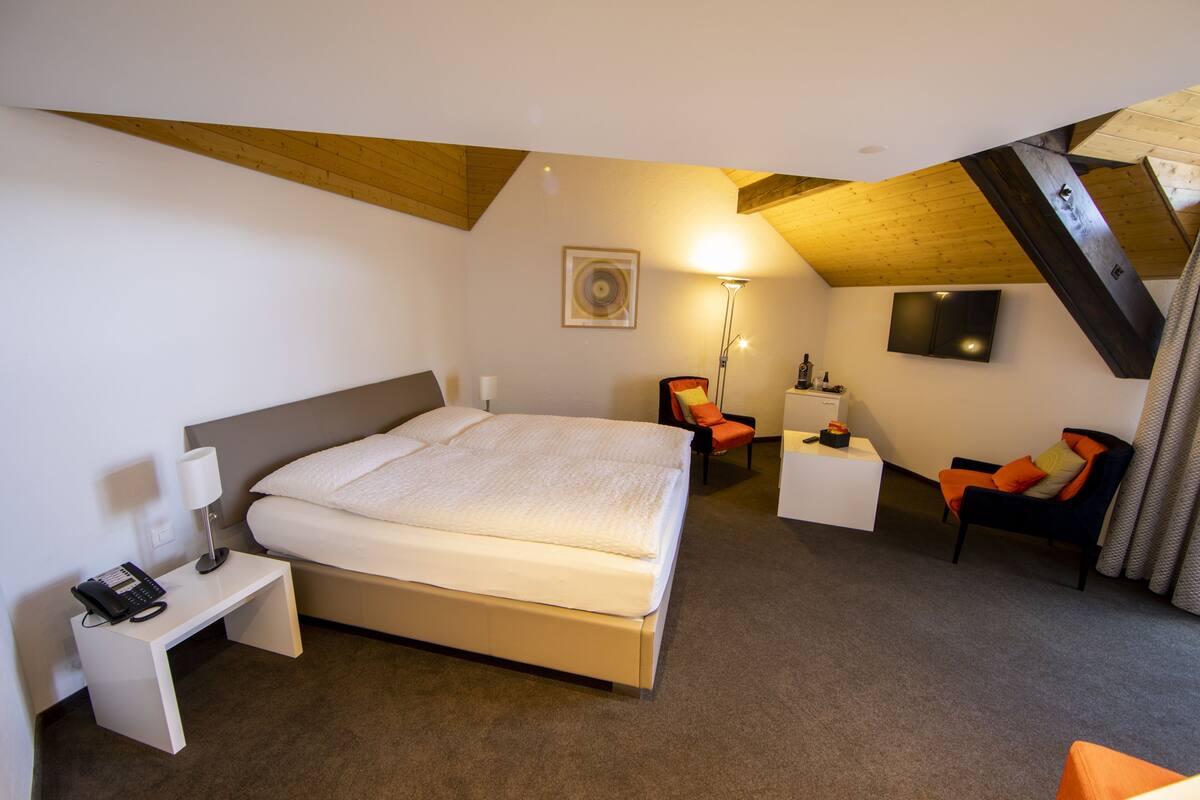 Een slaapkamer met een groot bed, een bureau, een stoel, een lamp en een televisie die aan de muur is bevestigd.
