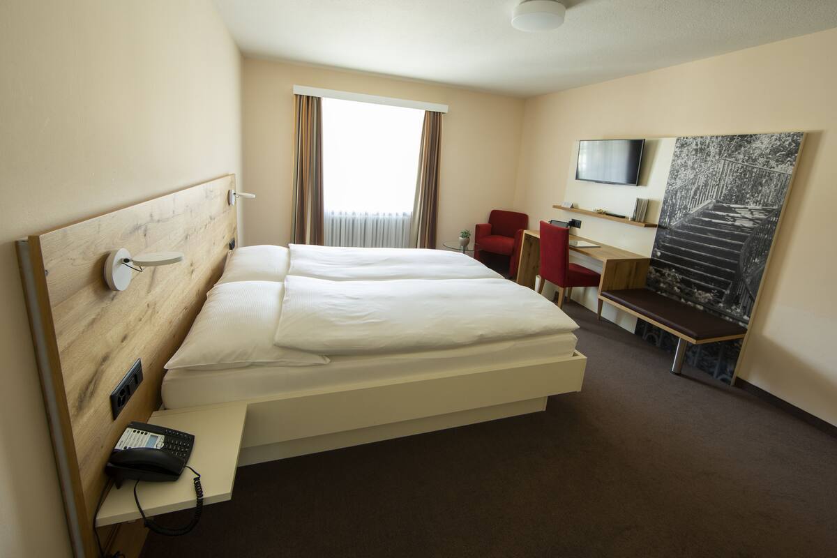 Een hotelkamer met een groot bed, een bureau, een stoel, een televisie en een schilderij aan de muur.