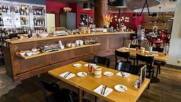 Interior de restaurante con barra, mesas de madera, sillas negras y una variedad de alimentos y bebidas a la vista.