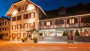 A traditional European hotel with a well-lit facade, a visible entrance, and a sign for a restaurant named "sattelschnecke".